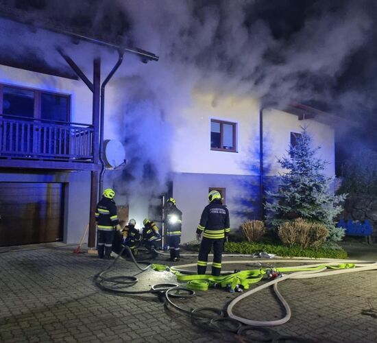 Feuerwehrleute bekämpfen einen Brand in einem Wohnhaus, während Rauch aus dem Keller dringt.