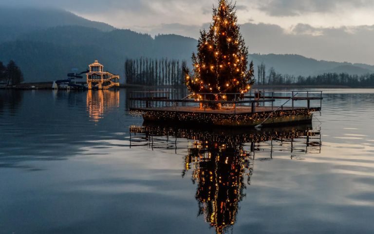 Foto: Ein geschmückter Weihnachtbaum auf einer Holzplattform im See vor Pörtschach