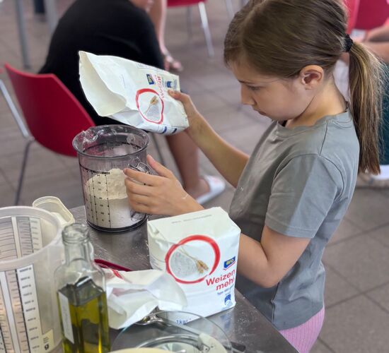 Ein Mädchen fügt Weizenmehl in eine Schüssel, während andere Kinder im Hintergrund warten. | © ARO