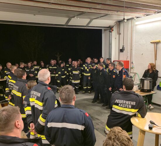 Eine große Gruppe von Feuerwehrleuten versammelt sich in einer Garage zur Besprechung bei Nacht.