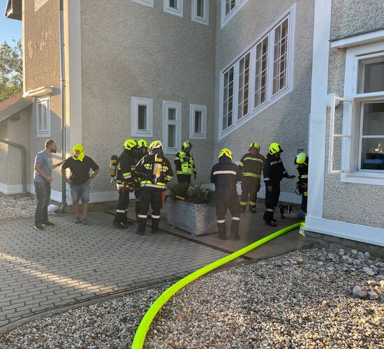 Feuerwehrleute besprechen sich vor einem Gebäude und bereiten sich auf einen Einsatz mit einem langen Schlauch vor.