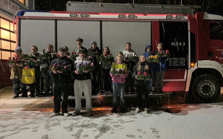 Eine Gruppe von Jugendlichen steht bei Schnee vor einem Feuerwehrauto und hält Adventskränze in den Händen.