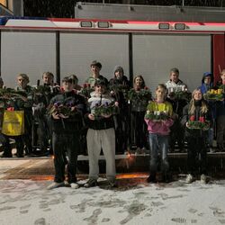 Eine Gruppe von Jugendlichen steht bei Schnee vor einem Feuerwehrauto und hält Adventskränze in den Händen.