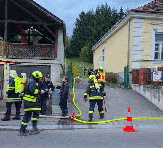 Feuerwehrleute bereiten sich auf einen Einsatz vor einem Gebäude mit einem Einsatzfahrzeug und Wasserschlauch vor.