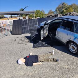 Ein Unfall-Szenario mit einem Auto, Solarzellen im Hintergrund und einer Puppe auf dem Boden dargestellt.