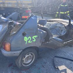 Ein schwer beschädigter blauer Wagen mit Nummer 925, umgeben von Einsatzkräften an einem Unfallort.
