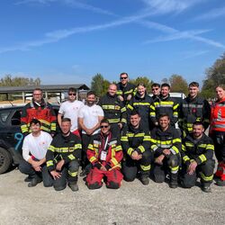 Eine Gruppe von Feuerwehrleuten posiert stolz vor einem Auto an einem sonnigen Herbsttag.