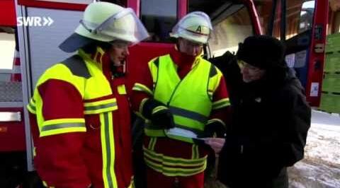Standbild aus dem Video mit einem Feuerwehmann, rechts daneben erklärt der Feuerwehkommandant einer Zivilperson etwas anhand eines Papieres