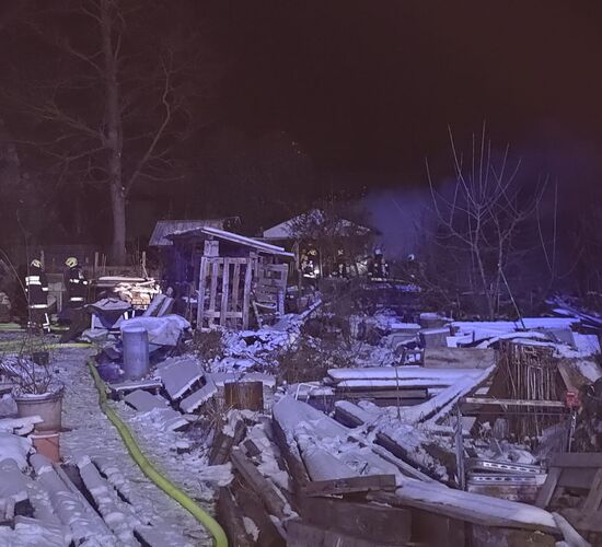 Feuerwehrleute löschen nachts im verschneiten Garten eine kleine Holzhütte