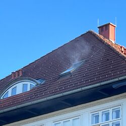 Rauch steigt von einem Dach mit Fenstern unter klarem Himmel auf, was auf eine mögliche Wärmequelle hinweist.