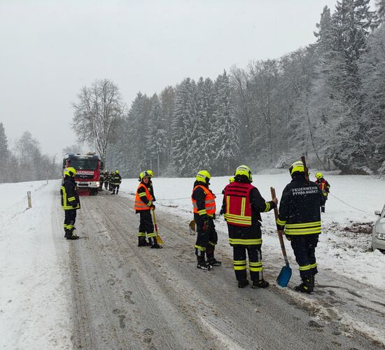Feuerwehrleute sichern eine verschneite Straße, während ein Auto im Graben liegt, um Hilfe zu leisten.