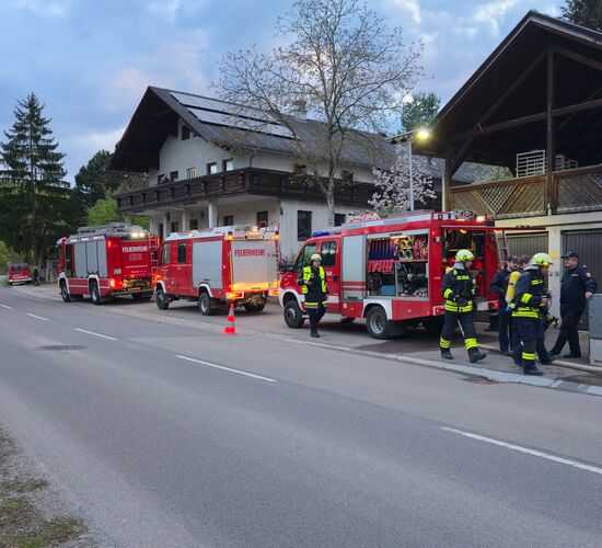 Feuerwehrleute arbeiten an einem Einsatz vor einem Gebäude, während Feuerwehrfahrzeuge bereitstehen.
