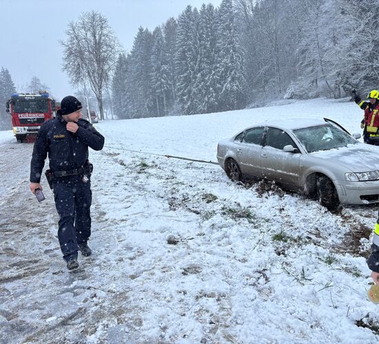 Ein Auto wird im Schnee von der Feuerwehr aus einem Graben gezogen, während ein Polizist den Einsatzort überwacht.