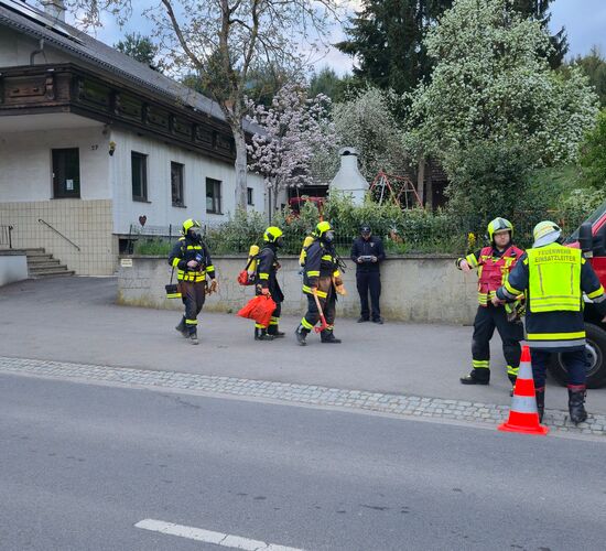 Feuerwehrleute in Schutzkleidung besprechen sich vor einem Einsatzfahrzeug neben einem Wohngebäude.