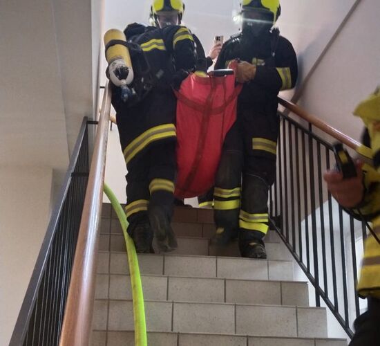 Feuerwehrleute tragen eine Person in einem roten Rettungsanzug die Treppe hinunter. | © Name