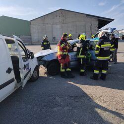 Feuerwehrleute helfen bei der Unfallrettung an einem beschädigten Fahrzeug auf einem Gelände.