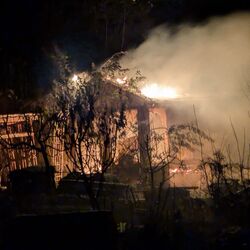 Ein Gebäude steht nachts in Flammen, während dichter Rauch in den dunklen Himmel aufsteigt.