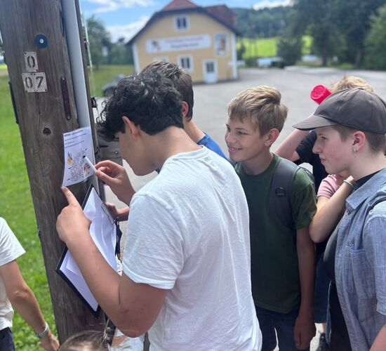 Eine Gruppe von Kindern untersucht eine Karte an einem Pfosten im Freien, um ihre nächste Aktivität zu planen.