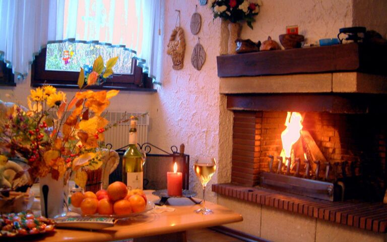 Offener Kamin Ein Teil eines festlich gedeckten Tisches, im Hintergrund brennen Holzscheite im Kamin