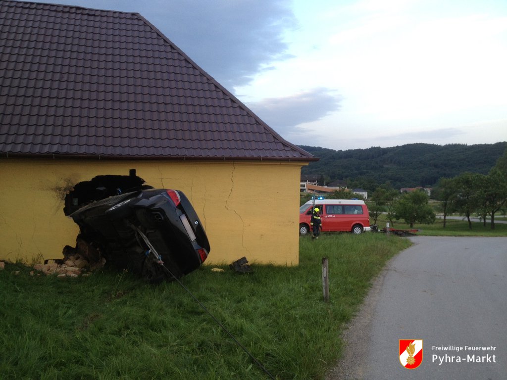 Foto: Das Fahrzeug auf der Seite liegend in der durchbrochenen Mauer